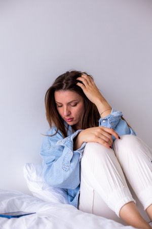 Pensive Woman in Casual Denim Shirt Sitting on Bedの写真素材