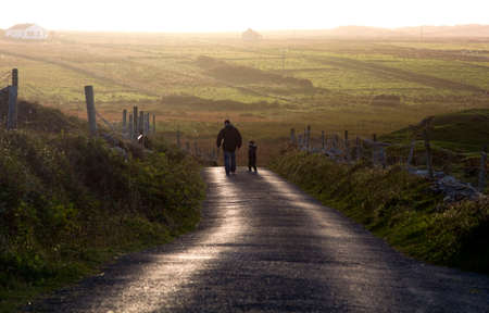 A man and a child walking along a country road at sunsetの写真素材