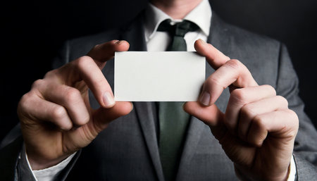 Businessman holding a blank business card on a dark background, close-upの素材