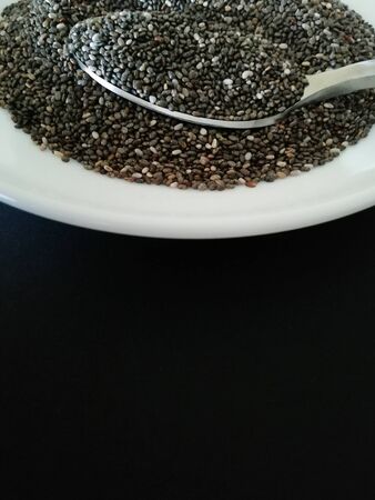 Chia seeds on a white plate on a black background.Copy spaceの写真素材