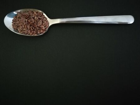 Flax seeds in the spoon on black background, vintage color toneの写真素材