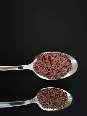 Flax seeds in the spoon on black background, vintage color tone. Copy spaceの写真素材
