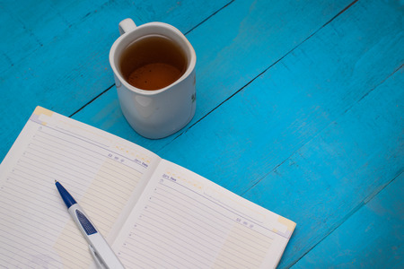 Cup of tea and a Notepad for taking notes on a blue wooden tableの写真素材