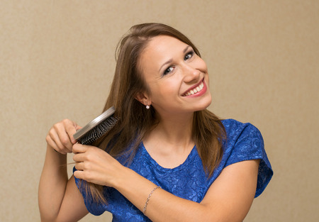 woman combing long brown hair comb and smiling , indoorsの写真素材