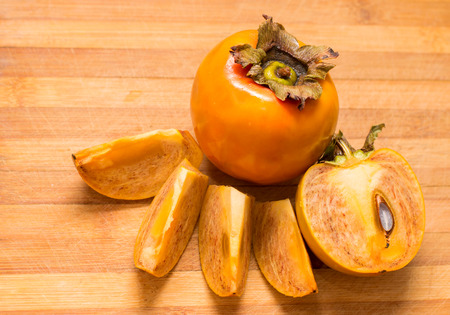 ripe persimmon and paper-thin slices on a wooden Boardの写真素材