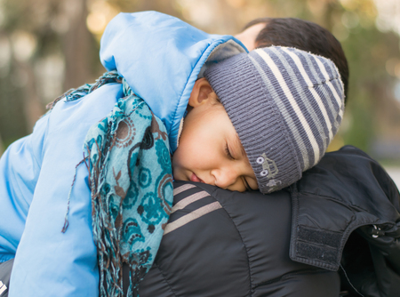 little boy sleeps on the shoulder of the dad outdoorsの写真素材