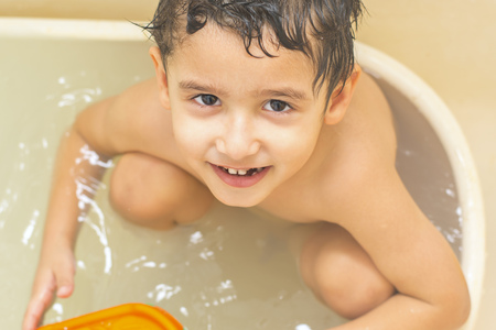 boy with brown eyes bathes alone in the tub and looks at the camera