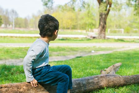 dark-haired boy sitting on a log aloneの写真素材