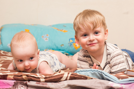 two blonde boys lie on the bed on his stomachの写真素材
