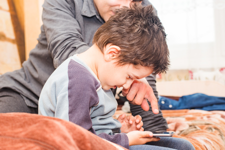 dark haired boy with dad playing in the phone in homeの写真素材