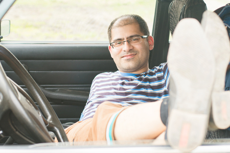 man resting in the car stretching his legs out of the car window