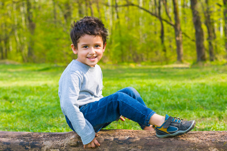 brown-eyed boy sitting on a log and smilingの写真素材