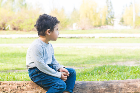 dark-haired boy sitting on a log aloneの写真素材