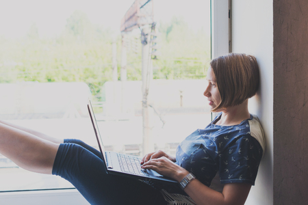 young woman freelancer with a laptop near the window. Toned.の写真素材