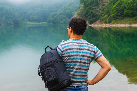 man with a backpack looking at a mountain lakeの写真素材
