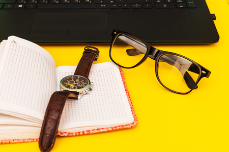 work table with laptop, glasses, clock and notebookの写真素材