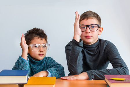 two boys in glasses holding hands up sitting at a Desk