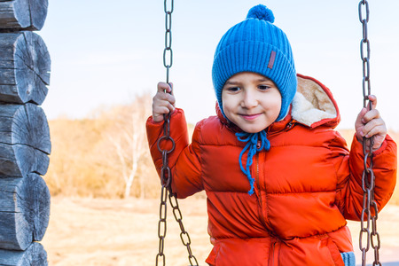 boy in an orange jacket swinging on a swing. rest in the villageの写真素材