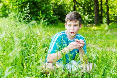 teen boy sitting in grass in summerの写真素材