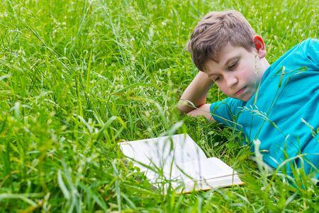 teen boy reading a book in nature in summerの写真素材