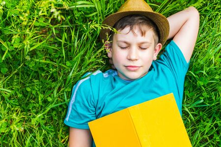 teenage boy fell asleep with a book on the grassの写真素材