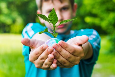 teen boy holding a globe from which a plant growsの写真素材