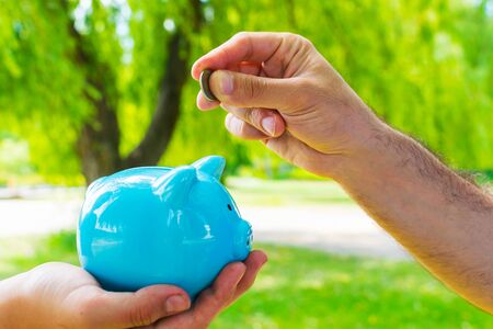 man's hand throws a coin into the piggy Bankの写真素材
