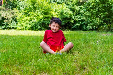 cheerful boy sitting on the grass in the summerの写真素材