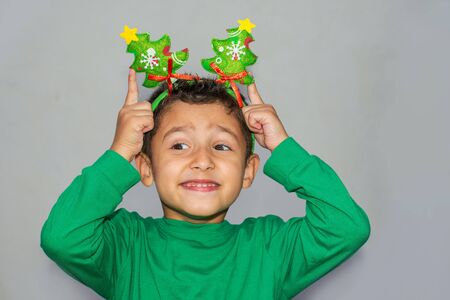 cheerful boy with the decoration of the Christmas tree on the head on gray backgroundの写真素材