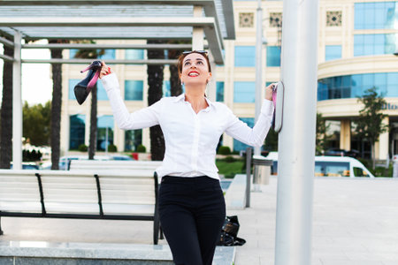 happy business woman carries shoes in her hand. A young free woman in the city.の写真素材