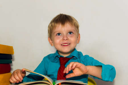 smiling preschool boy at the table reading a book
