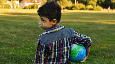 a little boy holds a globe in his hand in a meadow