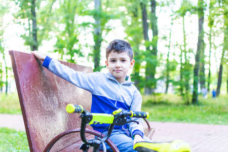 boy is sitting on a bench, and near his bikeの写真素材