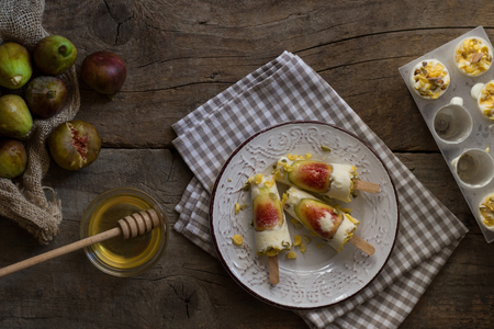 Ice cream pops made with fresh figs, Greek yogurt and sour cream in a plate on a rustic wooden table. Garnish with honey, cornflakes and pumpkin seed. Summer lifestyle. Preparing healthy dessert. Homemade product. Recipe ideas. Food photography.の写真素材
