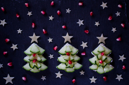 Creative and healthy snack for kids in shape of Christmas tree with cucumber, cheese and pomegranate seeds. Holiday breakfast table idea. New year dinner for children concept. Christmas food decoration.の写真素材