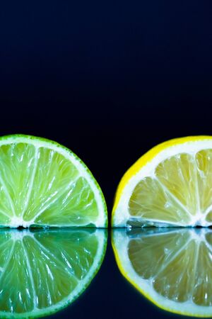 Lemon and lime slice on black reflective background. Creative food concept, minimal style. Copy spaceの写真素材