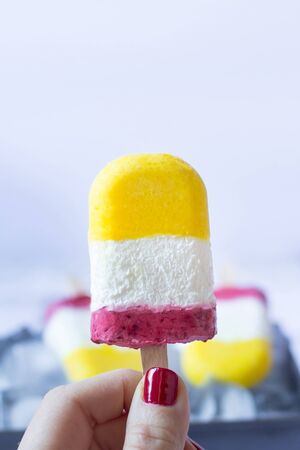 Ice cream pops made with mango, raspberry  and yogurt in woman hand. Summer refreshment. Homemade healthy dessert. Recipe ideas. Close upの写真素材