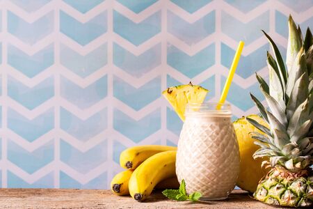 Fresh smoothie with banana and pineapple in decorative jar on wooden table. Healthy food for breakfast and snack. Summer refreshment. Copy spaceの写真素材