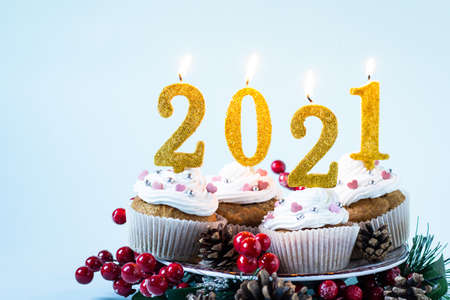 Happy New Year 2021 cupcakes with lighting candles on blue background. Merry Christmas and winter season greetings concept. Copy spaceの写真素材