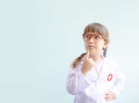 Kid playing doctor on light blue background with copy space. Cute girl in doctor or nurse uniform thinking .の写真素材