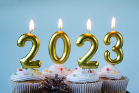 Happy New Year 2023 cupcakes with lighting candles on blue background. Merry Christmas and winter season greetings concept. Copy spaceの写真素材
