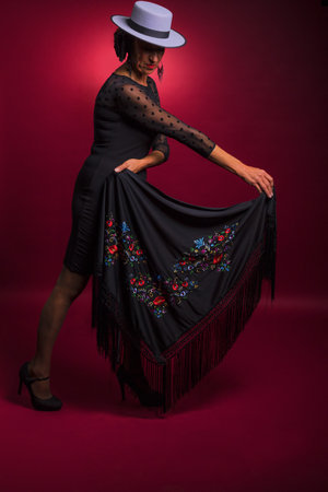 Beautiful young woman in black dress and hat posing on red backgroundの写真素材