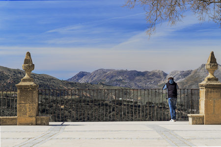 Pensively, a boy looks at the landscape, leaning on the railing, looking at the Serrania de Ronda from aboveの写真素材