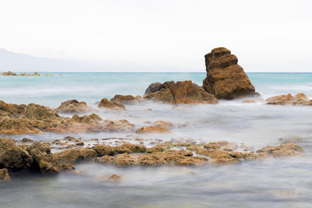 Tropical beach with rocks and turquoise water in cloudy dayの写真素材