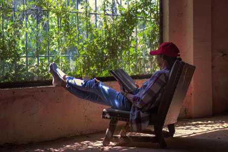 A woman sitting with her legs on the window, reading a book and having a coffee. Resting easy, on vacationの写真素材