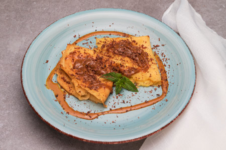 On a light blue plate we see two caramel sauce crepes sprinkled with chocolate and a few basil leaves.の写真素材
