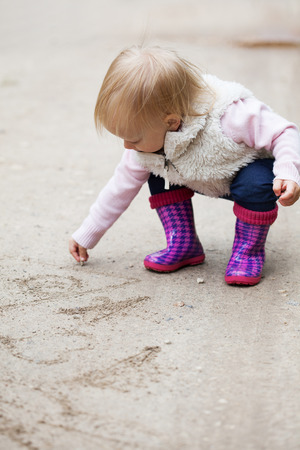 Happy smiling portrait of a 2 year old blonde girl drawing on the sand on natureの写真素材