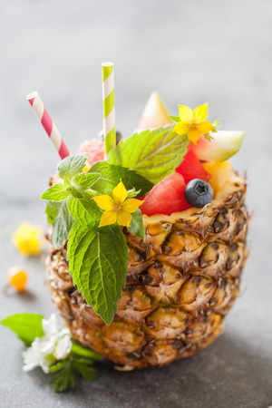 Exotic fruit salad served in half pineapple on dark background close upの写真素材