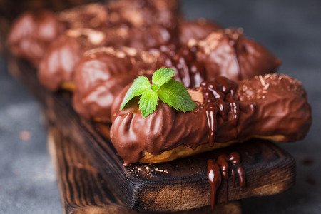 Chocolate eclair decorated with mint and melted chocolate on dark background