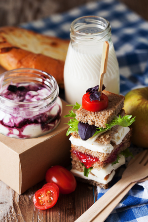 Healthy school lunch with a sandwich, fresh fruits, bun, blueberry yogurt and milk on rustic wooden background, close upの写真素材